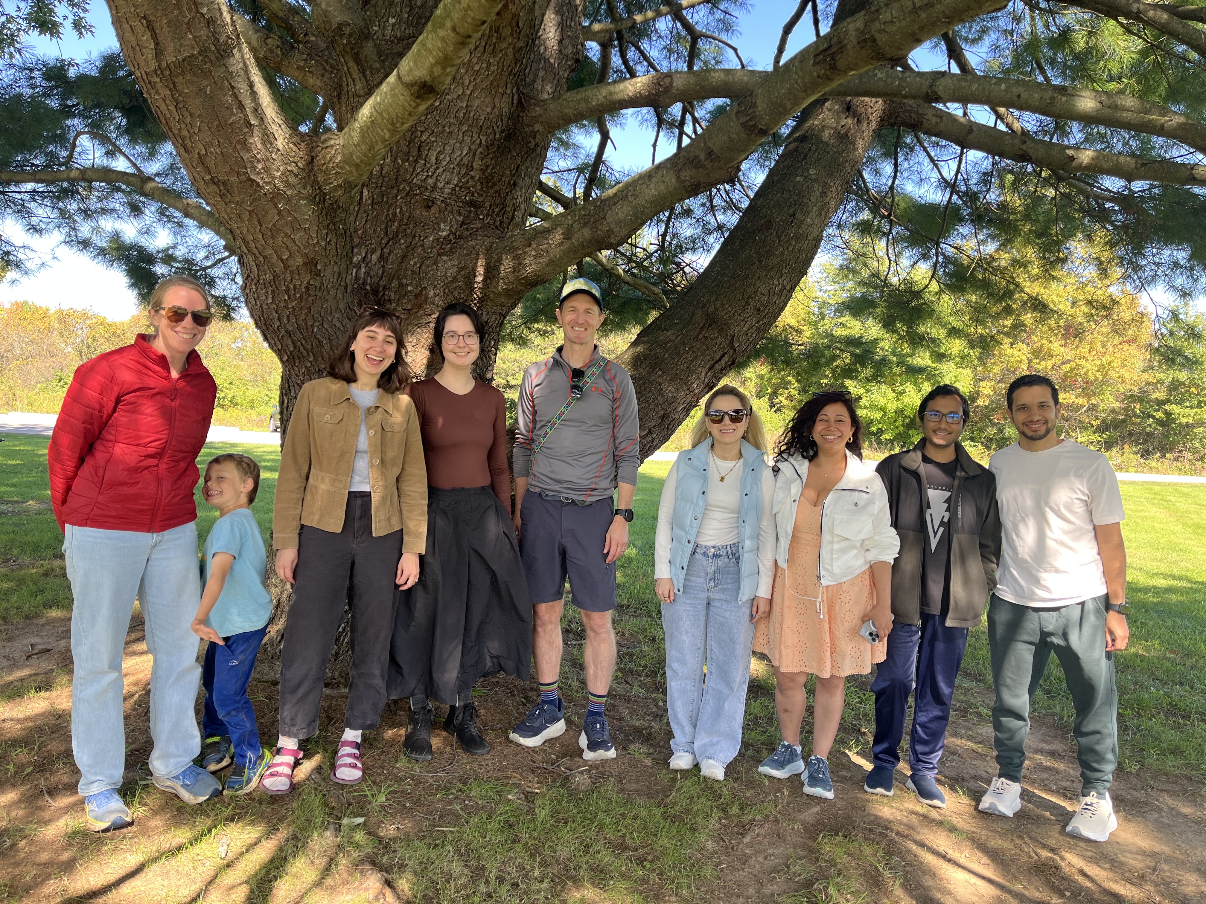 Lab members and family gathered beneath a pine tree at Walnut Woods Metro Park for Rebecca’s farewell picnic.